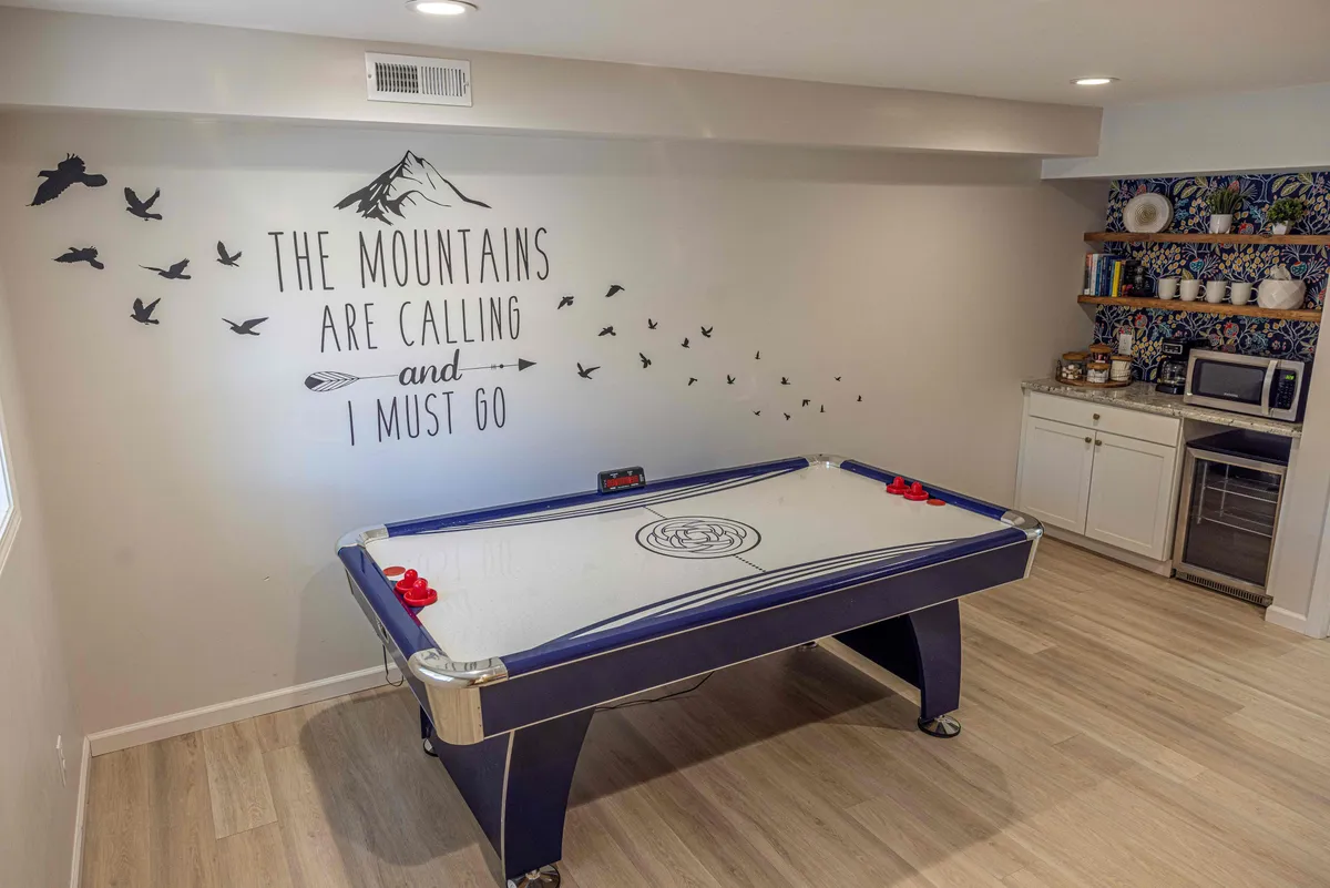 An interior activity area featuring an air hockey table in a playful, energetic setting. Decor includes a wall mural and a visible kitchen snack area, suggesting a space where families can gather for fun and games after their outdoor adventures.