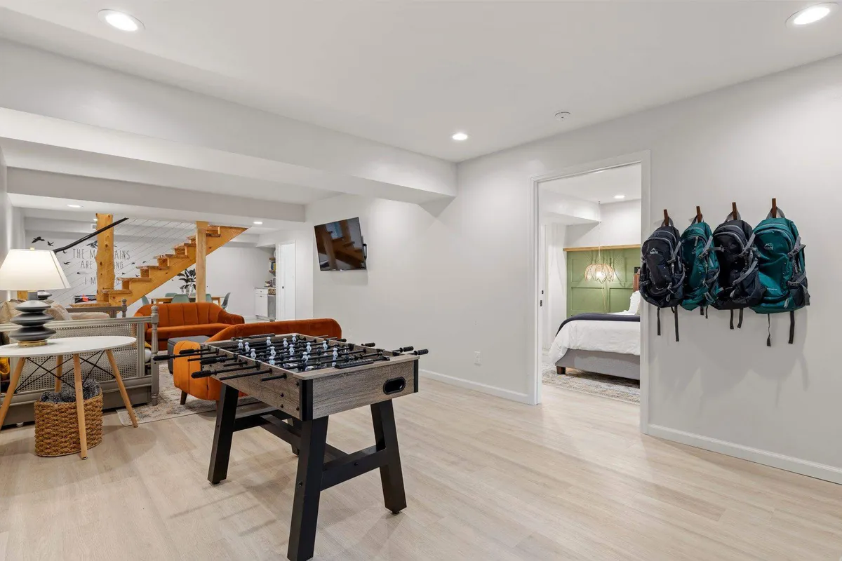 This scene includes a foosball table positioned near an orange sofa and a staircase, creating a relaxed, multifunctional living area. The space is inviting, comfortable, and clearly set up for both gaming and lounging.