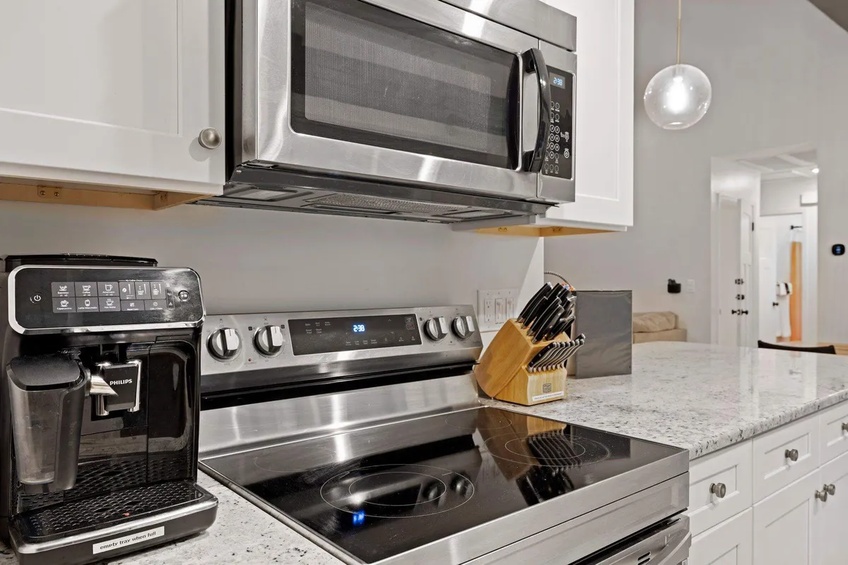A sleek, modern kitchen featuring stainless steel appliances, a granite countertop, coffee maker, and a knife block. The space is bright and functional, ideal for cooking and gathering. The coffee maker is prominently displayed, hinting at morning rituals and group coffee moments.
