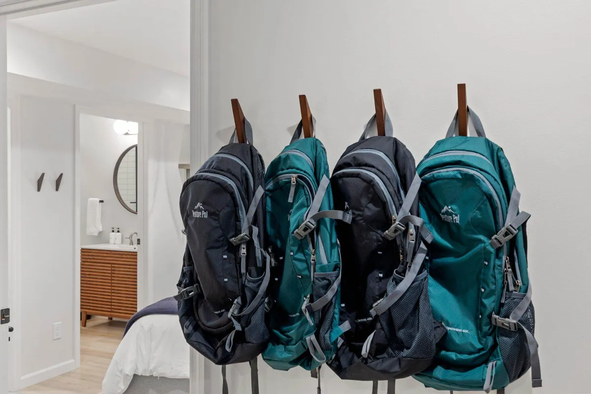 This image features three backpacks hanging on hooks beside a bathroom door and a wooden storage unit. The scene evokes a sense of adventure and active days spent outdoors, suggesting guests returning from explorations and preparing for new outings.