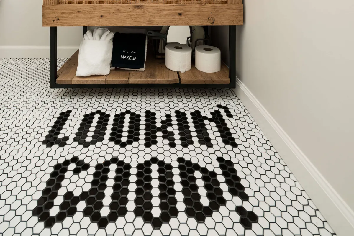 The image shows a bright, inviting bathroom scene with friends enjoying a light-hearted morning together. Visible are a stylish wooden vanity, plush towels, and playful text on the floor, all suggesting a warm and relaxing self-care routine before a day of exploring nearby attractions.