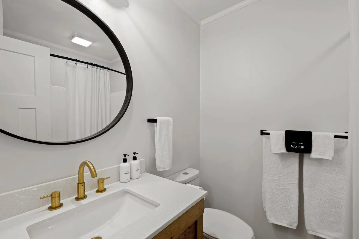 A modern bathroom featuring an oval mirror, gold faucet, sink countertop, and neatly folded towels. The setting is fresh and inviting, ideal for morning or evening self-care routines.