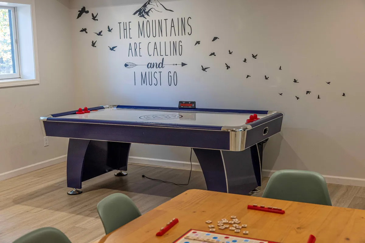A bright interior shot featuring an air hockey table, motivational wall art, and a sturdy wooden dining table. The room exudes energy and provides a seamless setting for both competitive games and group gatherings.