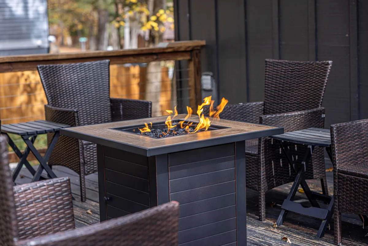 This exterior image showcases a cozy fire pit surrounded by chairs on a spacious deck, with the deck railing visible. The setting evokes a sense of communal gathering, perfect for relaxing with friends after a day of brewery hopping.