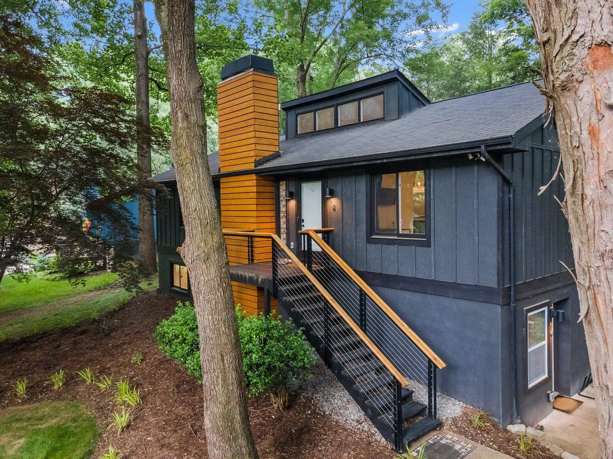 The exterior of a modern home with wood accents, surrounded by attractive landscaping. There’s a spacious deck visible, hinting at areas for barbecues, stargazing, and nature enjoyment. The setting is inviting and highlights the transition between the house and the outdoors.