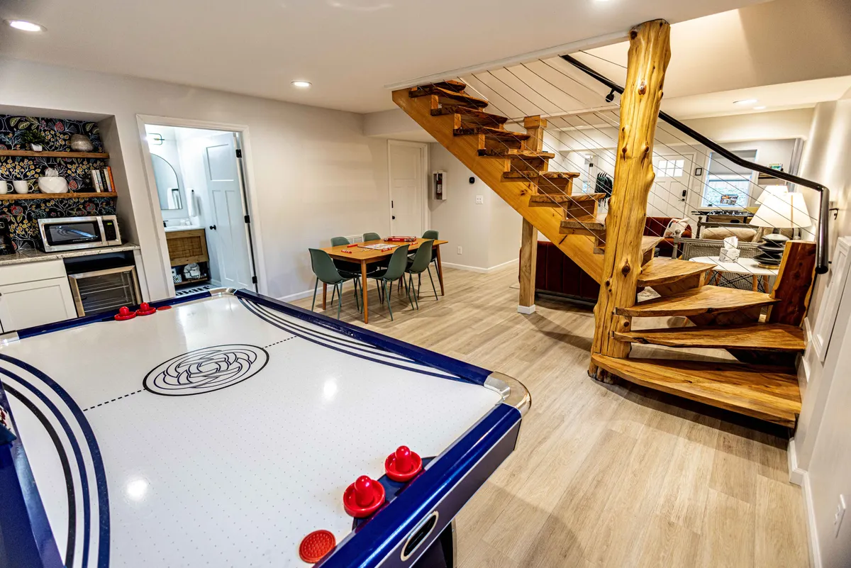 An inviting interior scene featuring an air hockey table, wooden staircase, and dining table. The space is designed for social activities, highlighting opportunities for friendly competition and shared meals among friends.